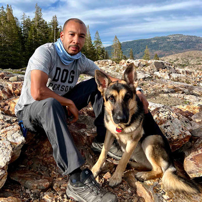 Man wearing Canina "Dog Person" Statement t-shirt sitting with German Shepherd dog on hike