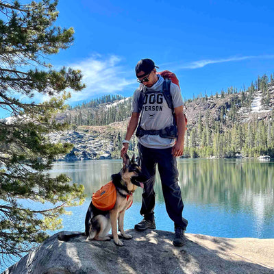 Man wearing Canina "Dog Person" Statement t-shirt standing with German Shepherd dog at lake