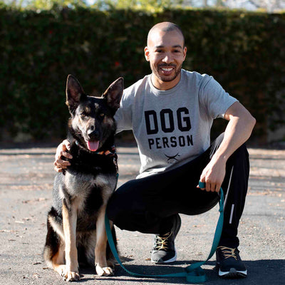 Man wearing Canina "Dog Person" Statement t-shirt crouching with German Shepherd dog before walk