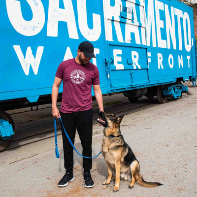 Man wearing Canina "Sactown" t-shirt standing with German Shepherd dog in front of train